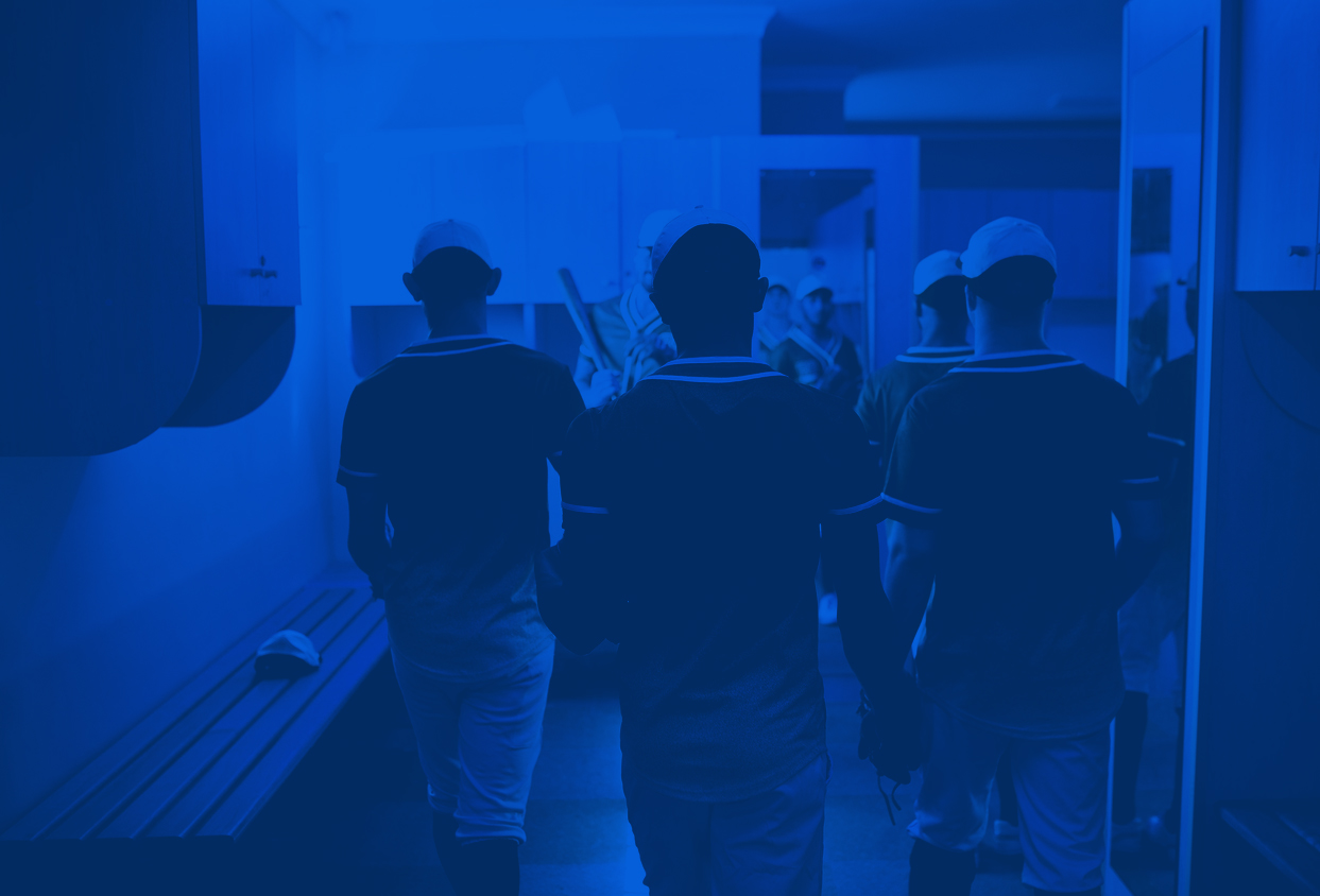Group of athletes in matching uniforms walking down a locker-room hallway, backs to camera amid blue lighting.